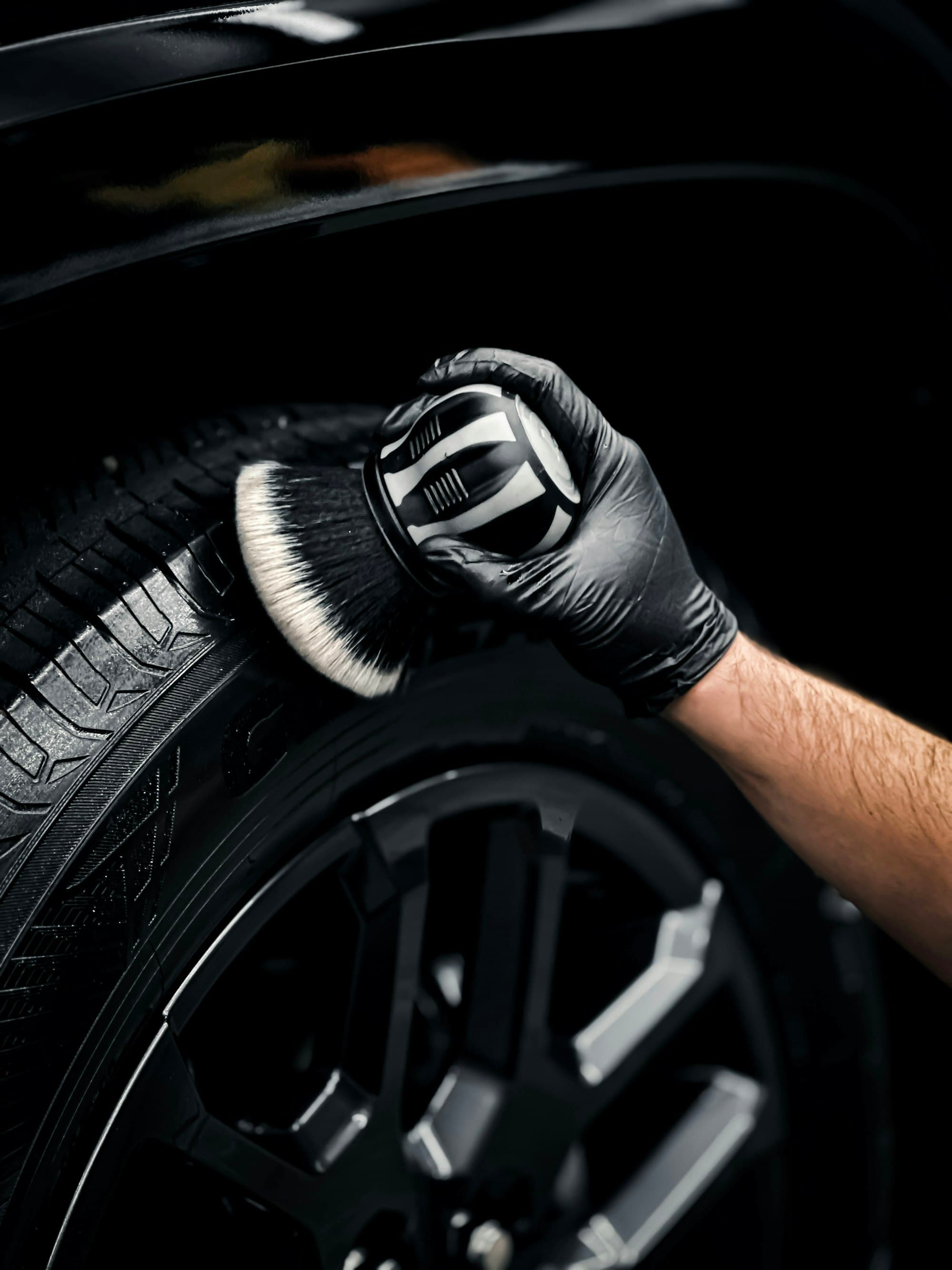 A gloved hand detailing a tyre with a soft brush