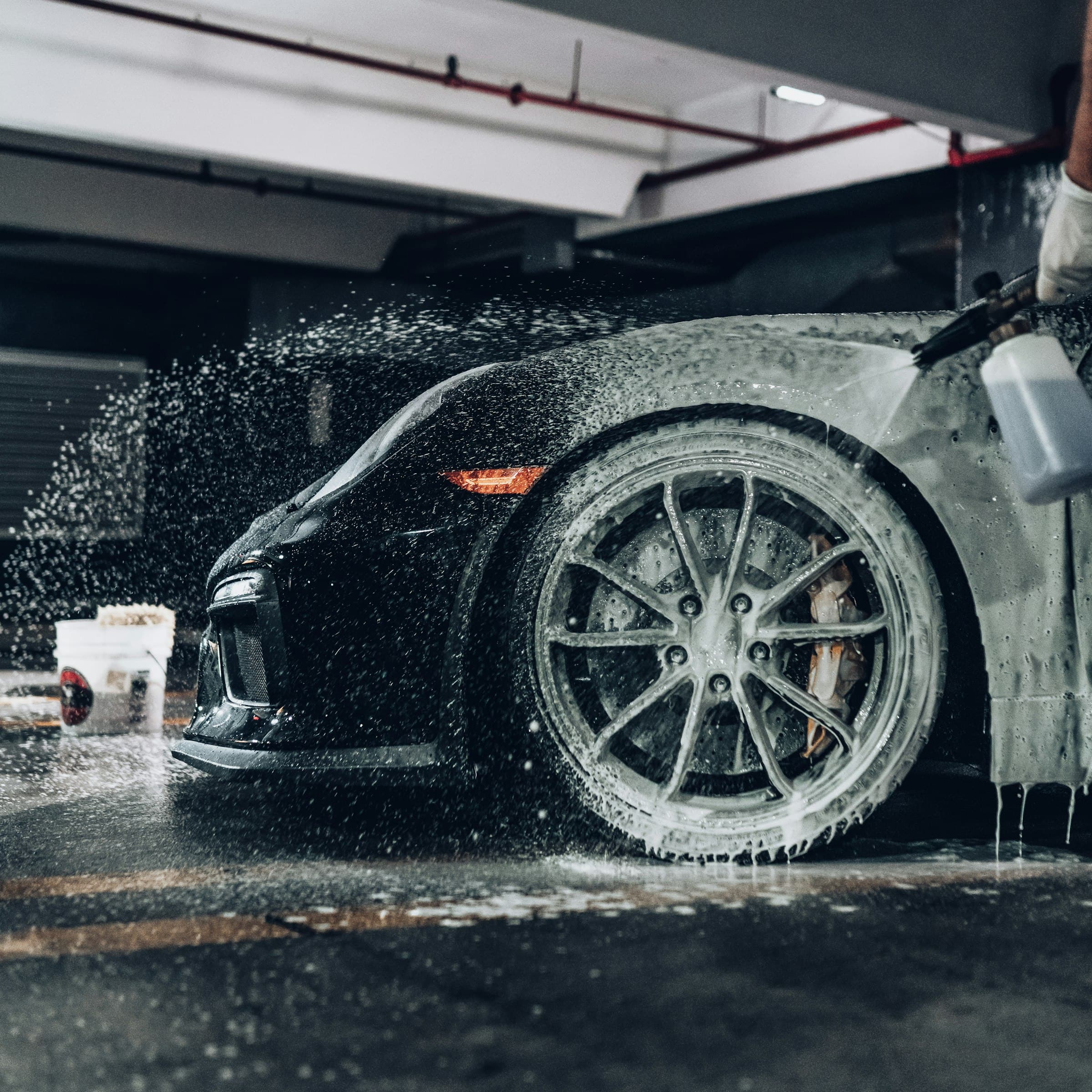 A black sports car covered in wash foam, wheel being rinsed