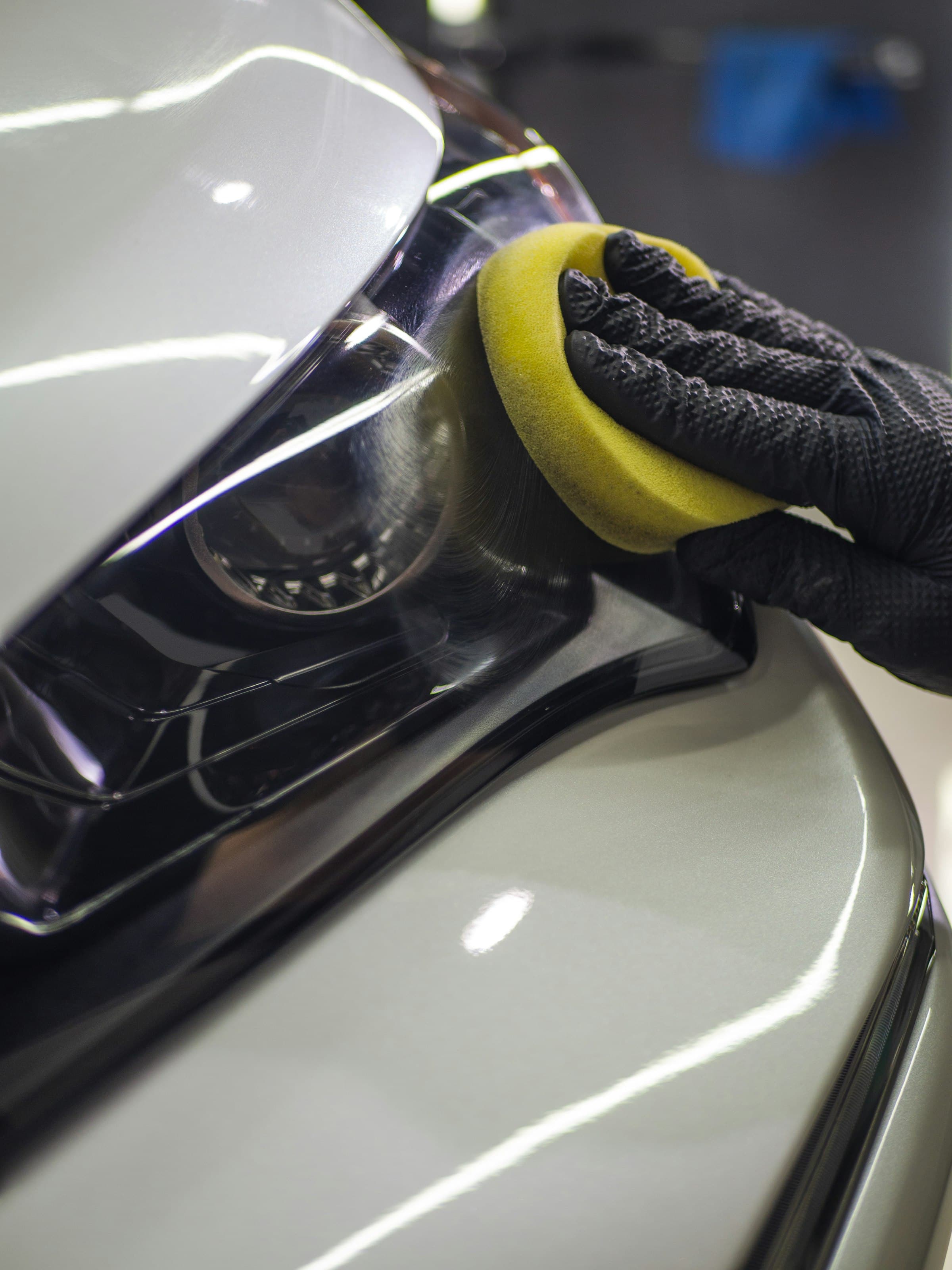 Coating being applied by hand to a white car beside the headlamp