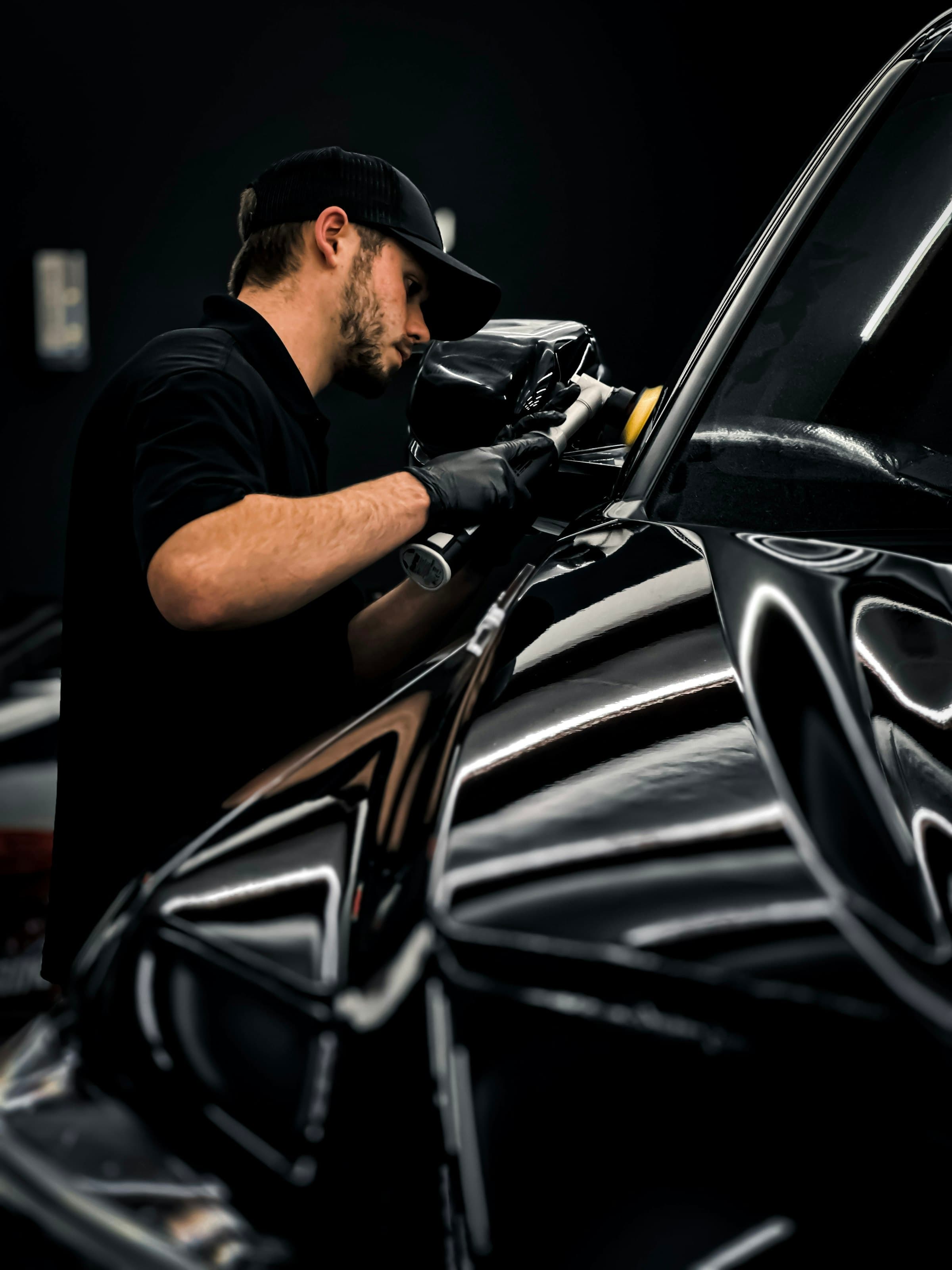 A detailer machine-polishing a black car in a dark studio