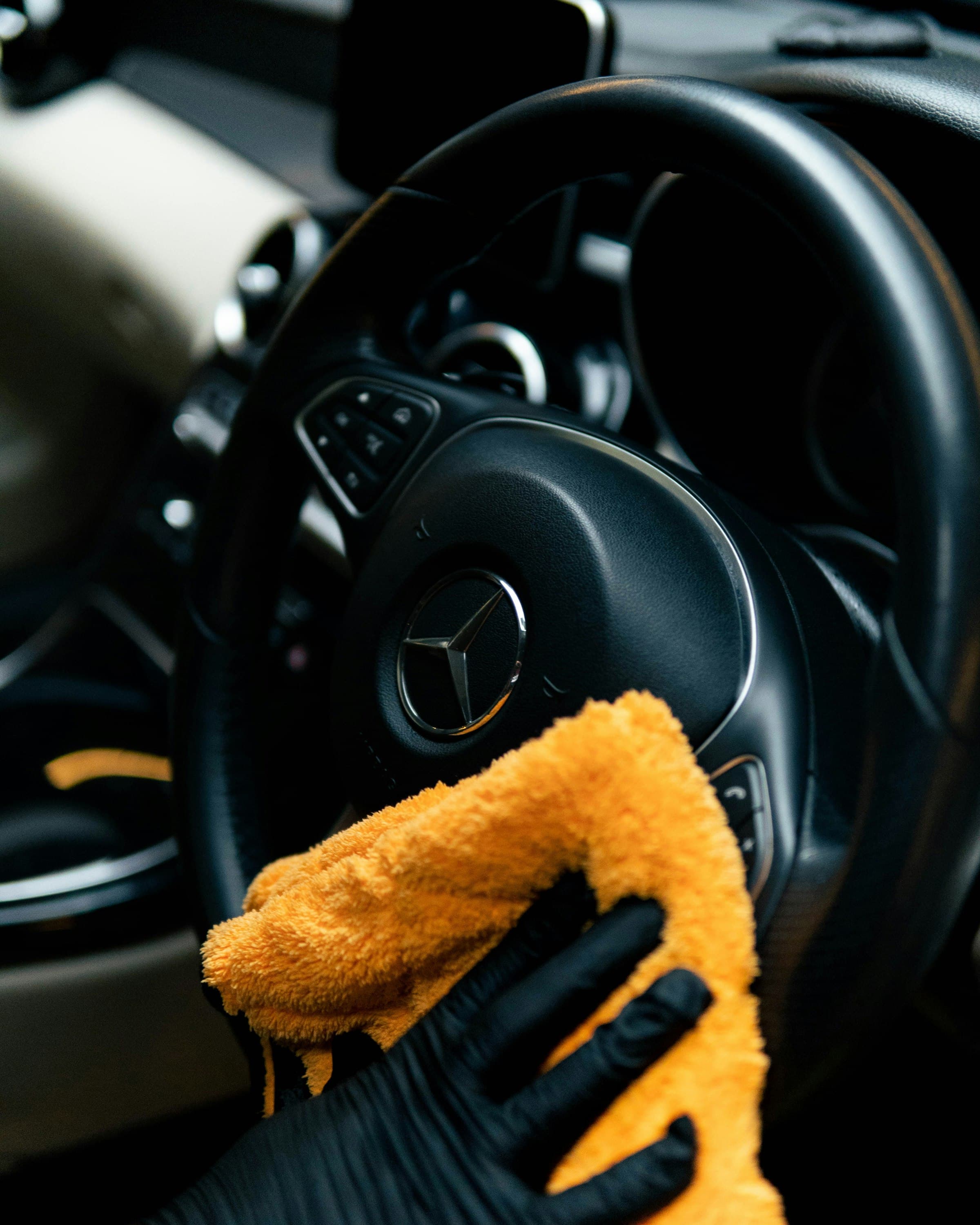A gloved hand wiping a steering wheel with a microfibre cloth